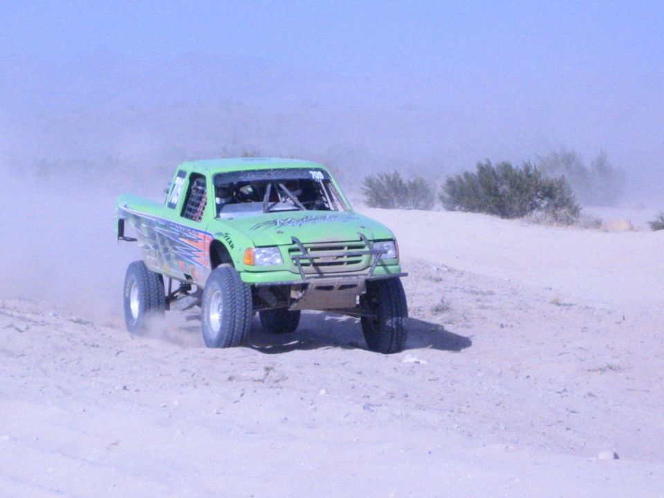 Green number-708 off-road race truck airborne over a sand dune