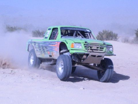 Green off-road race truck head-on jumping a sand rise in the desert