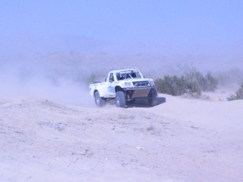 White off-road race truck on a sand dune in hazy desert terrain