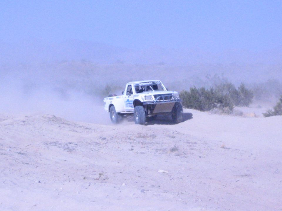 White off-road race truck on a sand dune in hazy desert terrain