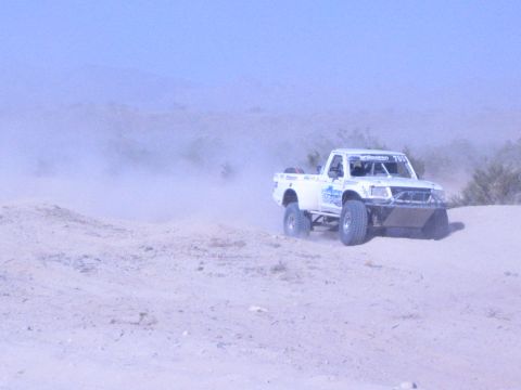 White off-road race truck at right of frame on dusty desert sand