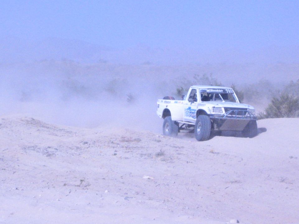 White off-road race truck at right of frame on dusty desert sand