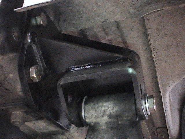 Black steel suspension bracket with poly bushing bolted to a truck frame
