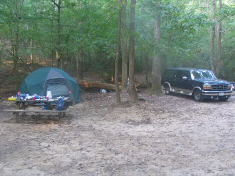 1995 Ford C-150 (Centurion Conversions) - A campsite scene features a tent and picnic table next to a dark blue Ford Bronco SUV.