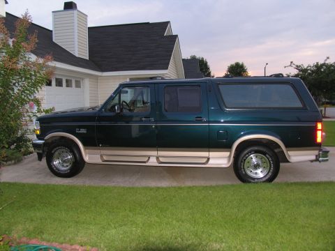 1995 Ford C-150 (Centurion Conversions) - Side view of a dark green Ford Bronco Centurion Conversion Van with tan trim, parked in front of a house.