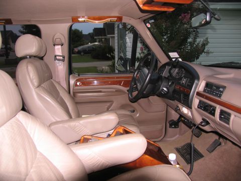 1995 Ford C-150 (Centurion Conversions) - Interior view of a van with captain's chairs and wood trim, showing the dashboard and steering wheel.