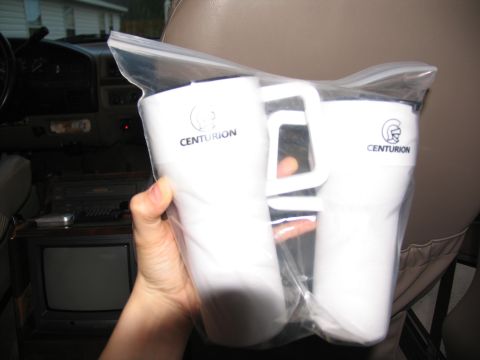 1995 Ford C-150 (Centurion Conversions) - Two Centurion travel mugs are held in front of a vehicle's interior, including a small TV.
