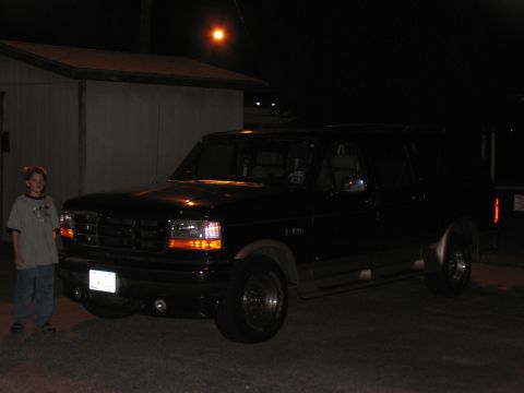 1995 Ford C-150 (Centurion Conversions) - A black 1995 Ford C-150 (Centurion Conversions) SUV is seen parked at night with a person standing beside it.