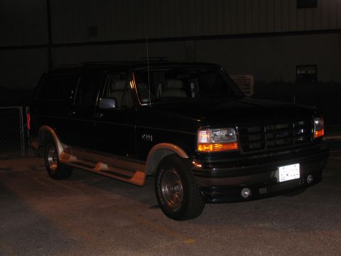 1995 Ford C-150 (Centurion Conversions) - This dark-colored Ford Bronco, woodgrain trim and running boards, is viewed from a three-quarter front angle at night.