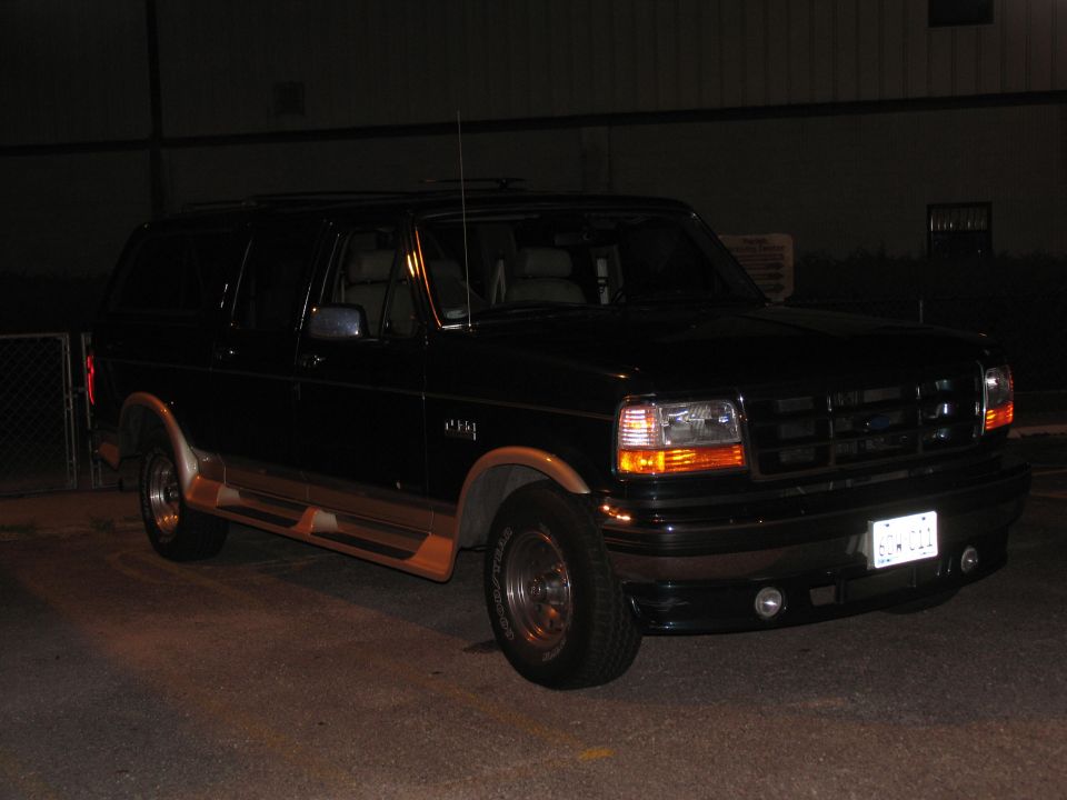 Black four-door Ford SUV conversion with tan cladding parked at night