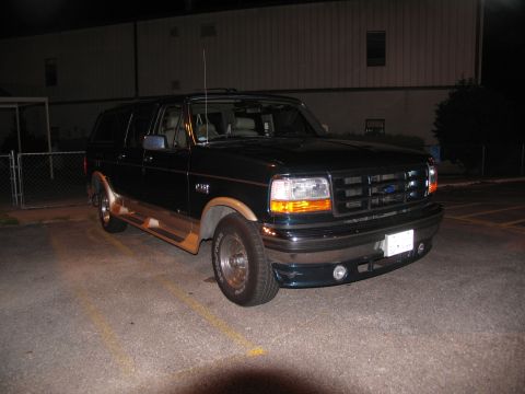 1995 Ford C-150 (Centurion Conversions) - A dark green Ford Bronco is parked in a lot at night, showing its front three-quarter view.