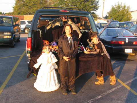 1995 Ford C-150 (Centurion Conversions) - Children in costumes at a Halloween trunk or treat event, with a green SUV and other vehicles in the background.