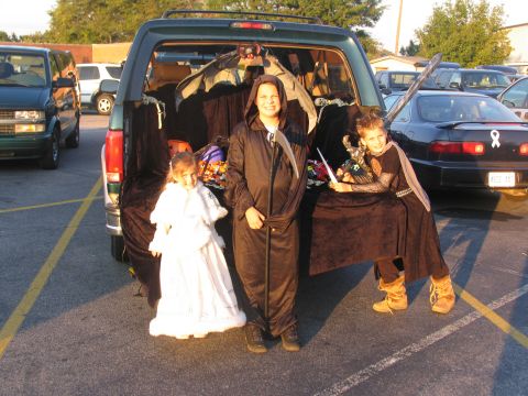 1995 Ford C-150 (Centurion Conversions) - Children in Halloween costumes gather around a decorated vehicle trunk, ready for trick-or-treating.
