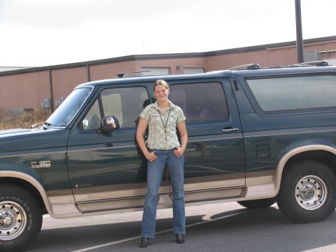 1995 Ford C-150 (Centurion Conversions) - Green Ford Bronco with tan trim, side view. A woman stands next to it.