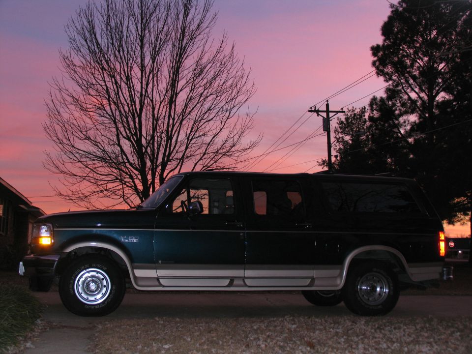 Side view of dark green and tan extended SUV with a bare tree and sunset sky