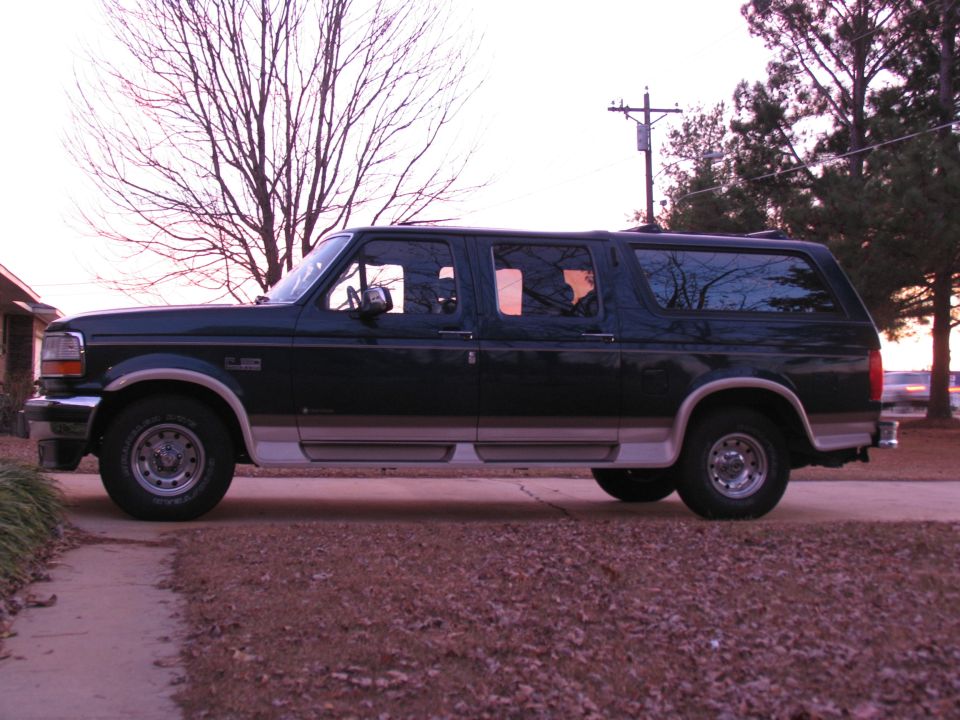 Teal and tan four-door Ford Bronco C-150 conversion SUV, driver side profile in driveway