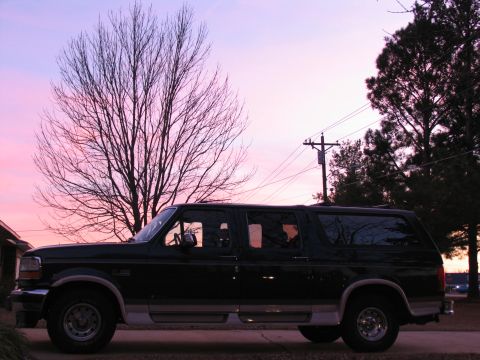 1995 Ford C-150 (Centurion Conversions) - A dark-colored Ford Bronco SUV is parked outside with a colorful sunset in the background.