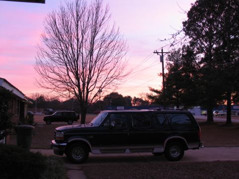 1995 Ford C-150 (Centurion Conversions) - A dark-colored Ford Bronco SUV is parked in a driveway during a colorful sunset.