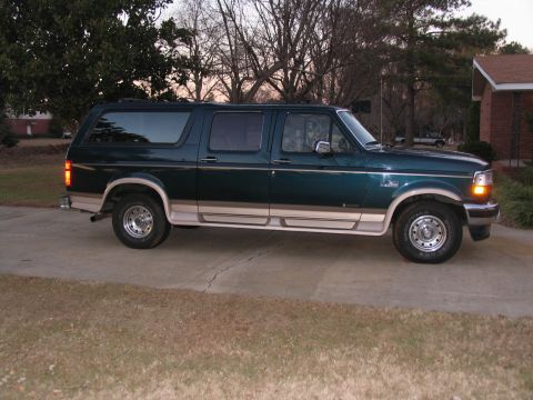 1995 Ford C-150 (Centurion Conversions) - A dark green Ford Bronco SUV with tan trim is parked on a concrete driveway in front of a house.