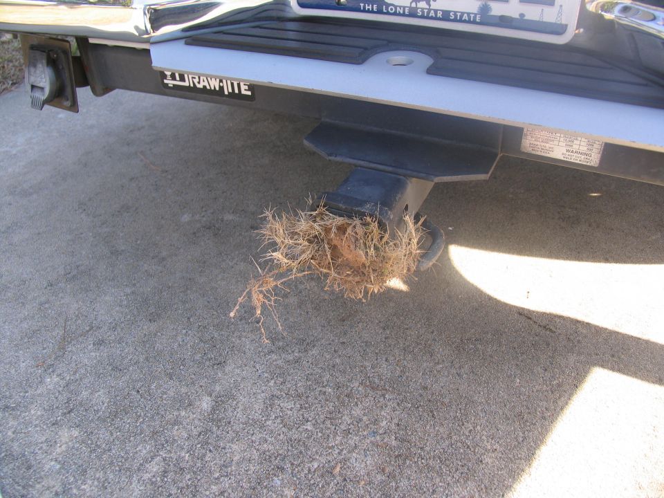 Trailer hitch with grass clump, "RAW-ITE" logo visible on bumper