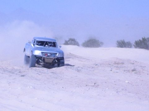 Silver number-708 off-road race truck on a dusty desert sand course