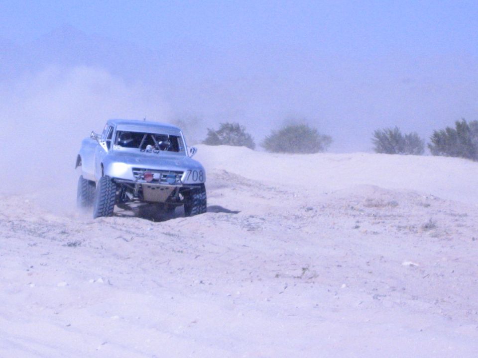 Silver number-708 off-road race truck on a dusty desert sand course
