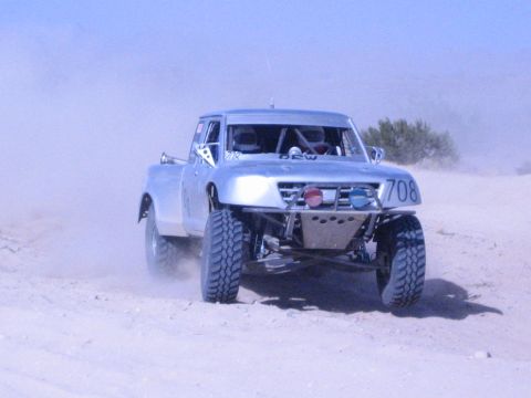Silver number-708 off-road race truck head-on kicking up sand
