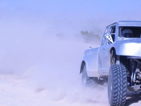 Silver number-708 off-road race truck side view in heavy dust