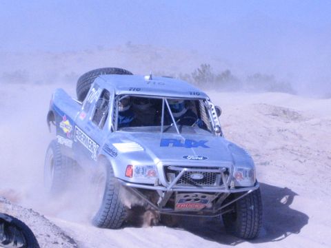 Silver Ford off-road race truck number 710 with FOX livery racing through desert sand