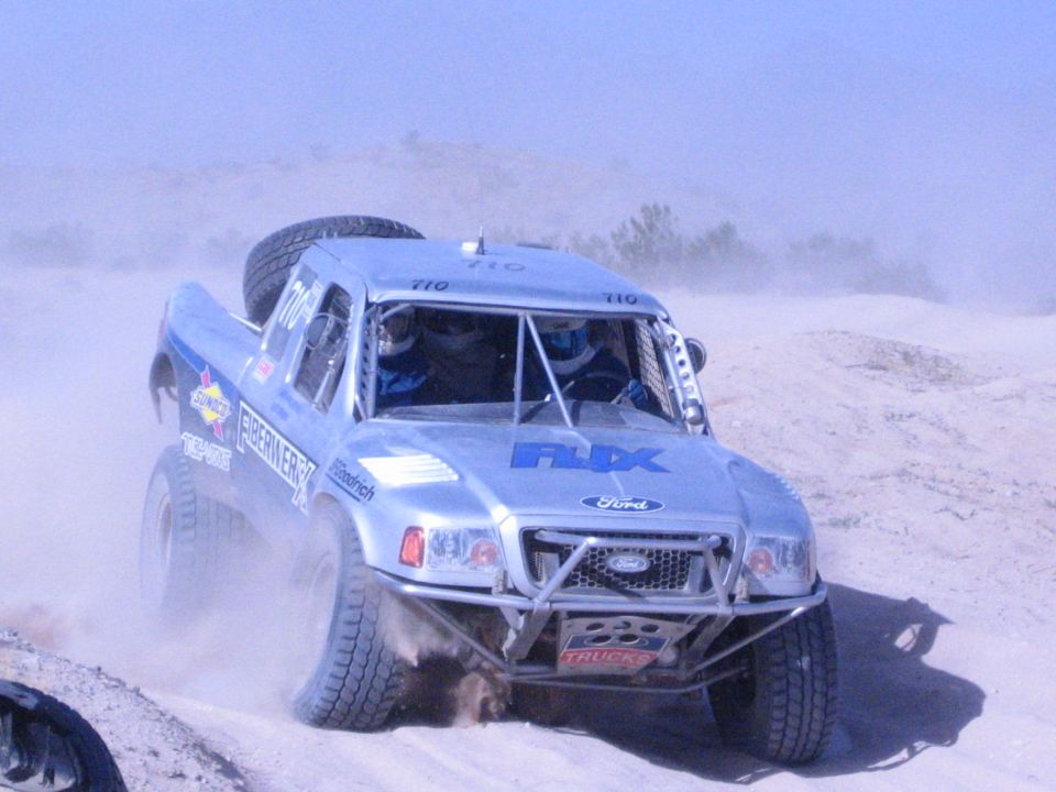 Silver Ford off-road race truck number 710 with FOX livery racing through desert sand