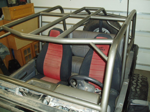 Bare metal roll cage and red-and-black seats inside a stripped Jeep tub in a garage