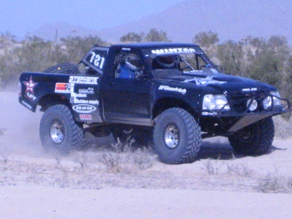 Black off-road race truck number 721 racing through scrubby desert terrain