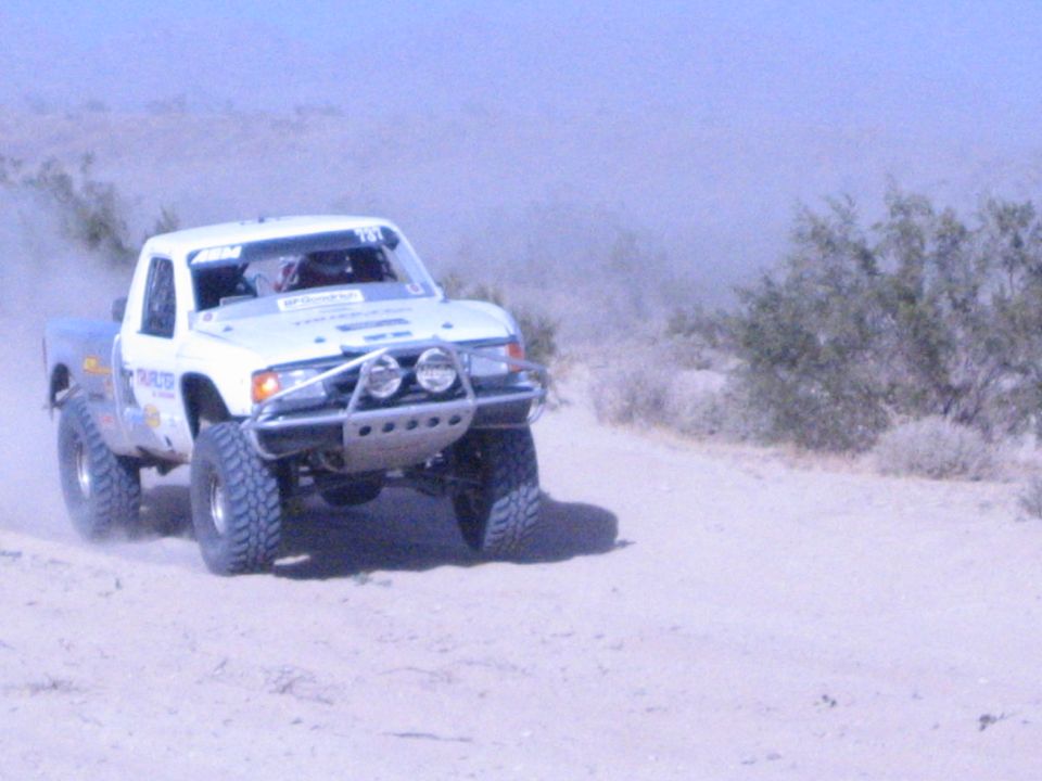White off-road race truck cornering on a dusty desert track with brush