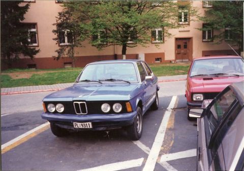2003 Jeep TJ - A blue sedan is parked in a lot next to other vehicles.