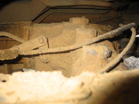 1995 Ford Bronco - Underside view of a heavily mud-caked transfer case and associated linkage.