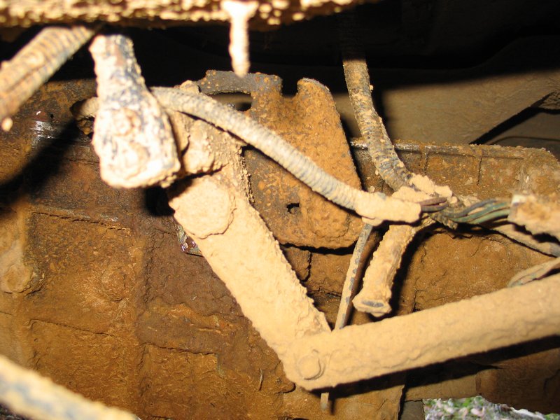 Close-up of rusty, mud-caked linkage and wiring under a vehicle