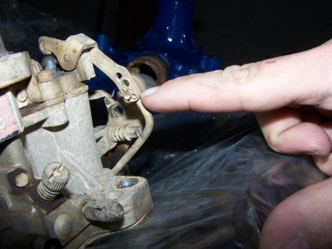 1979 Ford F-150 - A finger points to the linkage of a carburetor, which appears to be dirty and used.