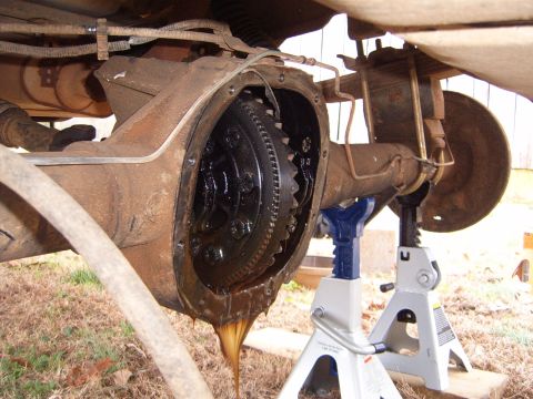 1988 Ford Bronco - The rear differential is open, showing gears and old fluid leaking out. The vehicle is supported by jack stands.
