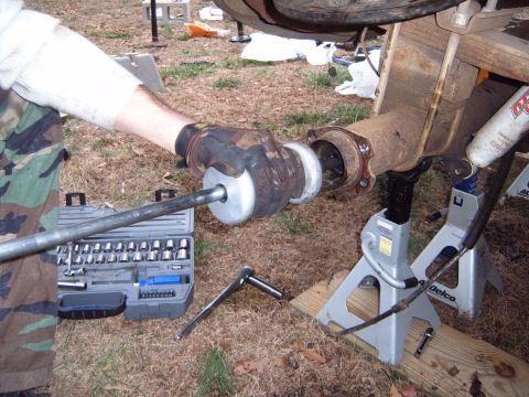 1988 Ford Bronco - A person uses a tool to work on a vehicle's rear axle assembly, supported by jack stands.