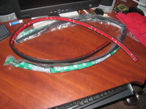 1991 Ford Bronco - Weather stripping with red adhesive backing is laid out on a wooden desk next to a computer keyboard and monitor.