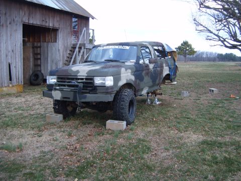 1988 Ford Bronco - Camouflaged 1988 Ford Bronco undergoing repairs outside a wooden barn.