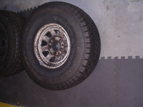 1985 Ford Bronco - Two tires and rusty wheels are shown on a grey floor.