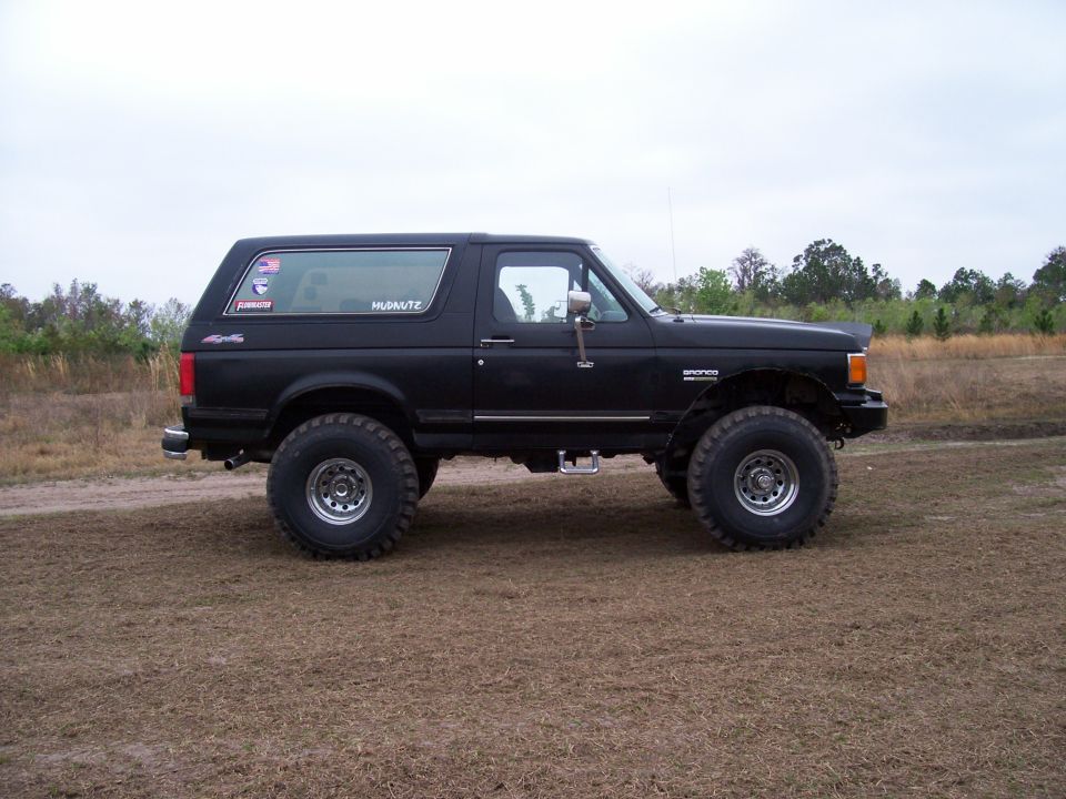 Black full-size Ford Bronco on a lift kit and large tires parked in a grassy field