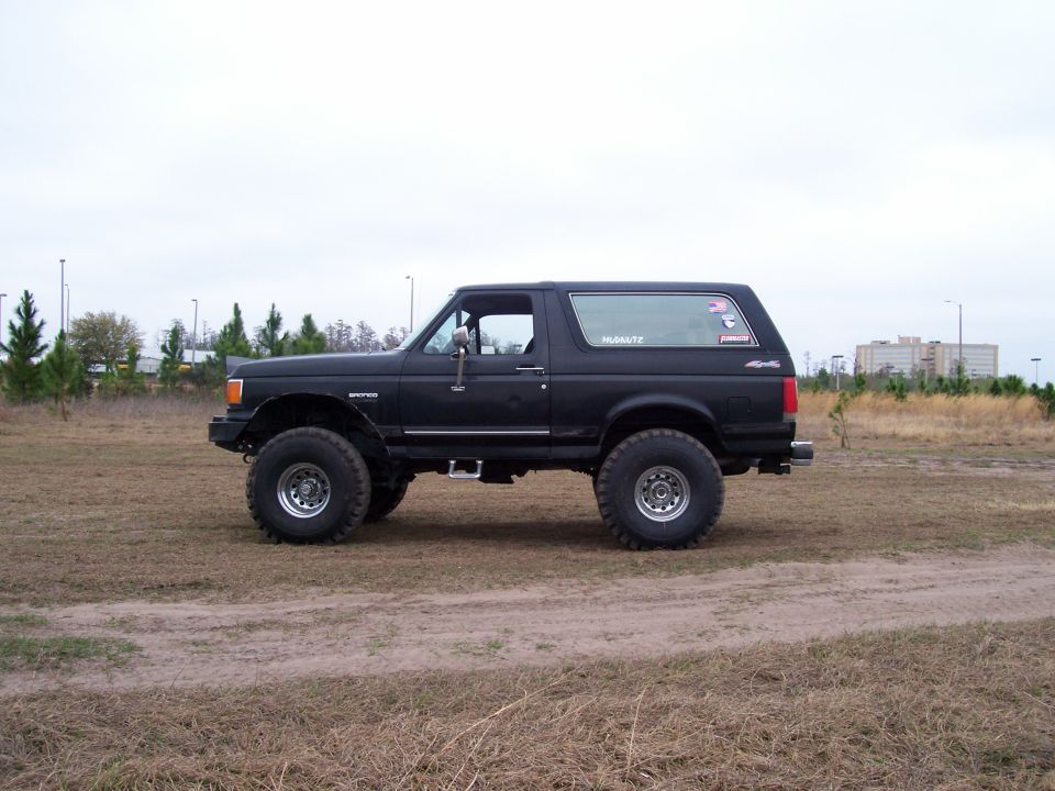 Side profile of a tall lifted black Ford Bronco on oversized tires in a field