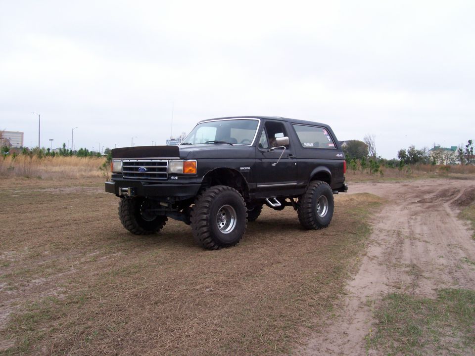 Front three-quarter of a lifted black Ford Bronco 4x4 with brush guard in a field
