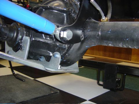 1990 Ford Bronco - Underside detail of a vehicle showing a polished aluminum skid plate and blue shock absorber over a checkered shop floor.