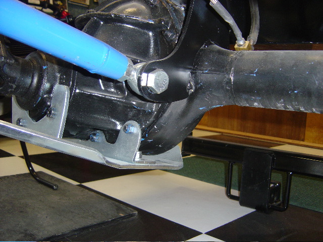 Underside of a vehicle showing skid plate and blue shock over a checkered floor