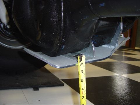 1990 Ford Bronco - yellow tape measure gauges ground clearance of an aluminum skid plate mounted under a black axle on a checkered floor.