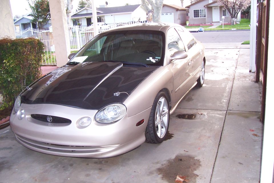 Gold sedan with a black hood, modified front bumper, and aftermarket wheels parked in a driveway