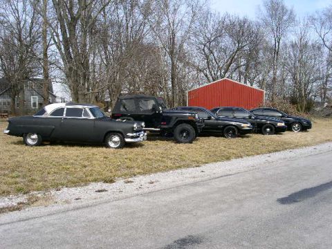 2001 Ford Crown Victoria - Several vehicles are parked on a grassy area next to a red barn.